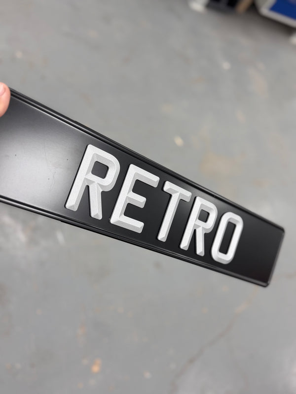 Black sign with 'RETRO' in white letters held by a hand on a gray floor.