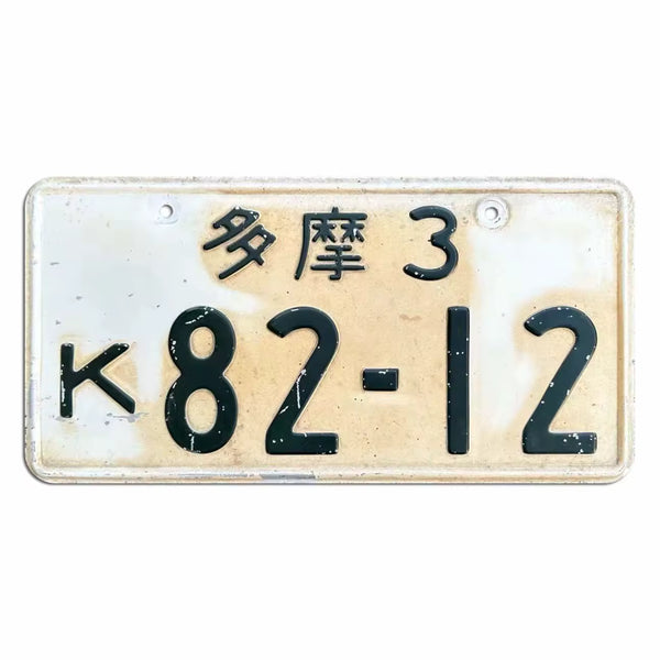 A vintage Japanese license plate with a cream-colored background, black characters, and weathered details. The plate features the characters '望尺3' and the numbers 'K82-12'.