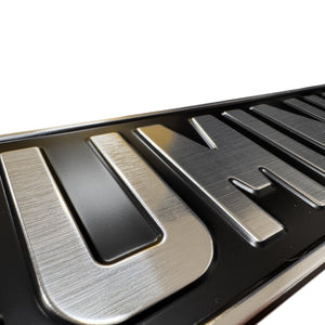 Close-up of brushed silver raised letters on a black metal pressed number plate