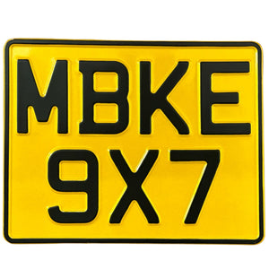 Yellow pressed metal motorbike number plate with black text displaying the characters MBKE 9x7.