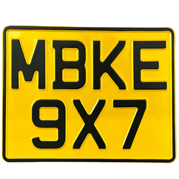 Yellow pressed metal motorbike number plate with black text displaying the characters MBKE 9x7.